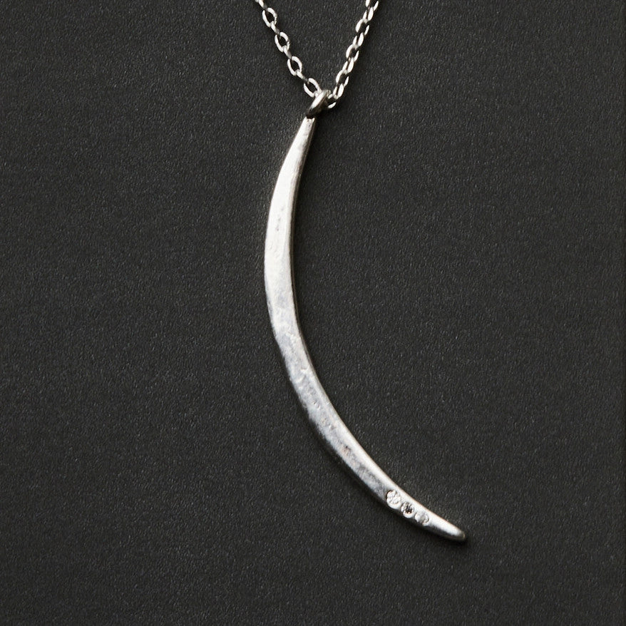 a slender silver pendant in the shape of a slice of the moon in its gibbous phase with 3 mini CZ stones on the bottom curve