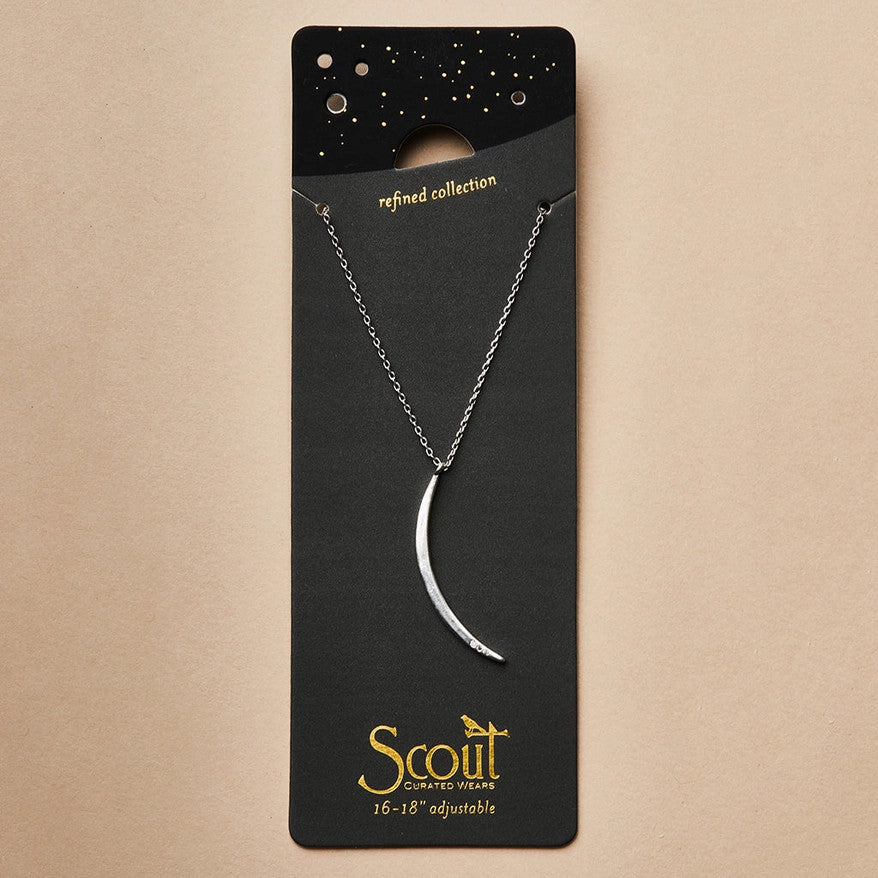 a slender silver pendant in the shape of a slice of the moon in its gibbous phase with 3 mini CZ stones on the bottom curve on a black card that serves as its packaging and shows more of the chain length