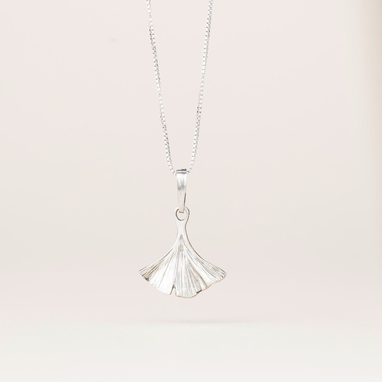 an intricately detailed pewter ginkgo leaf shaped pendant hanging from a silver chain
