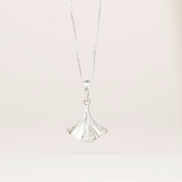 an intricately detailed pewter ginkgo leaf shaped pendant hanging from a silver chain