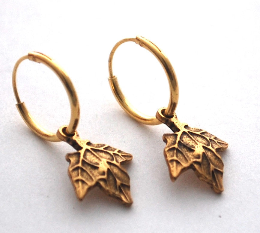 close up of gold maple hoop earrings on a white surface