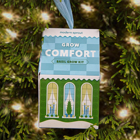 the Grow Comfort - Basil ornament hanging from an evergreen tree with twinkle lights