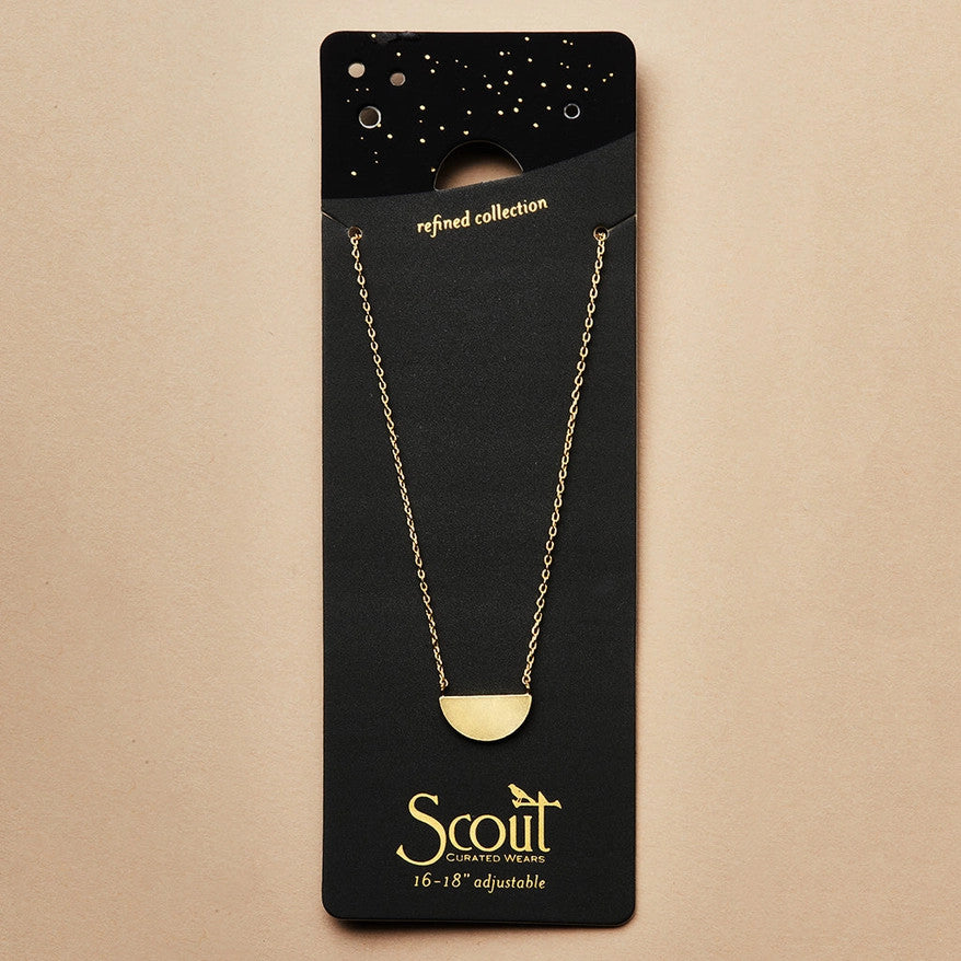 A gold necklace with a half moon pendant on a black card that it is packaged with