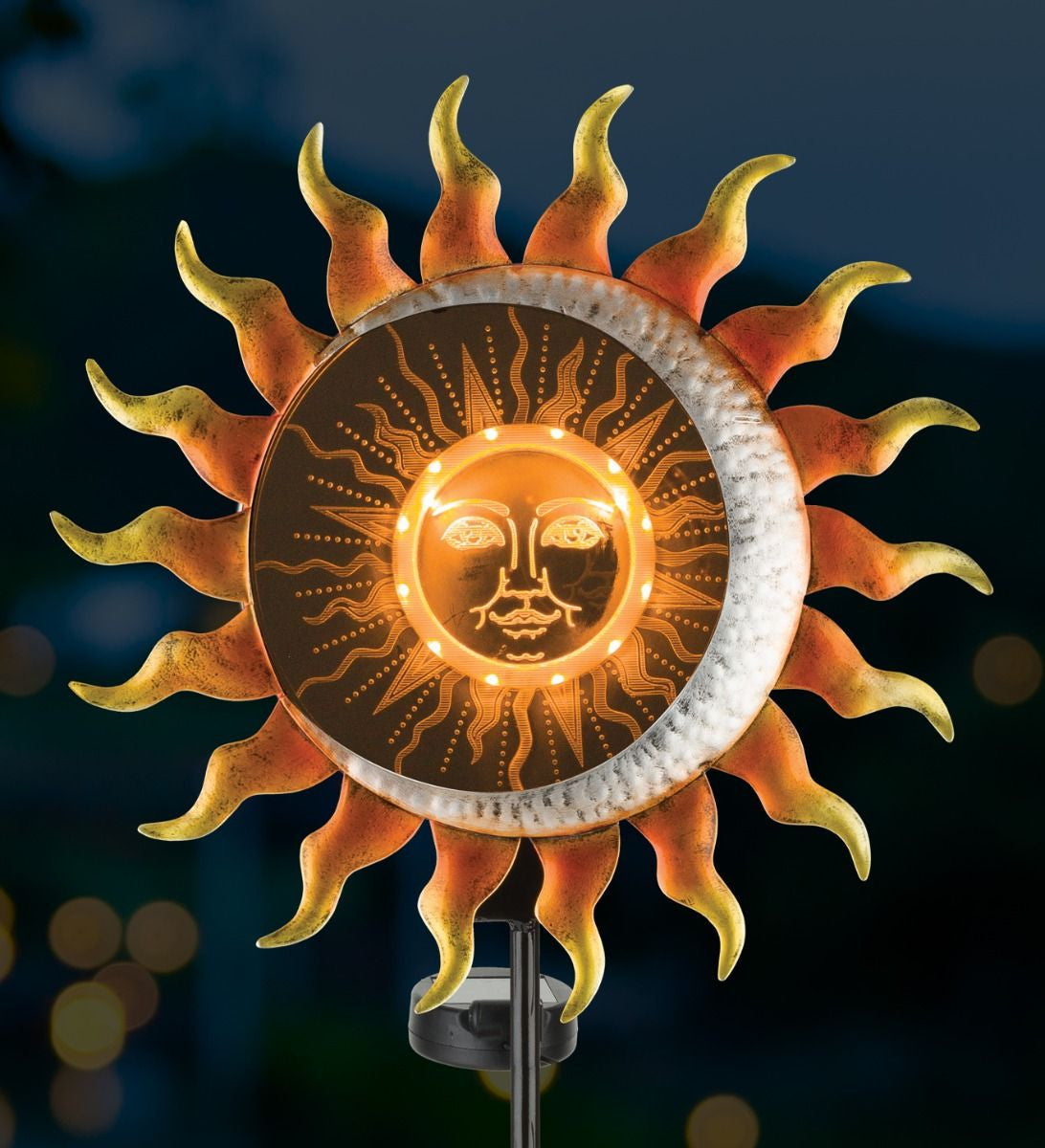 Illusion solar stake glowing at night, displaying the illuminated sun design with amber lights.