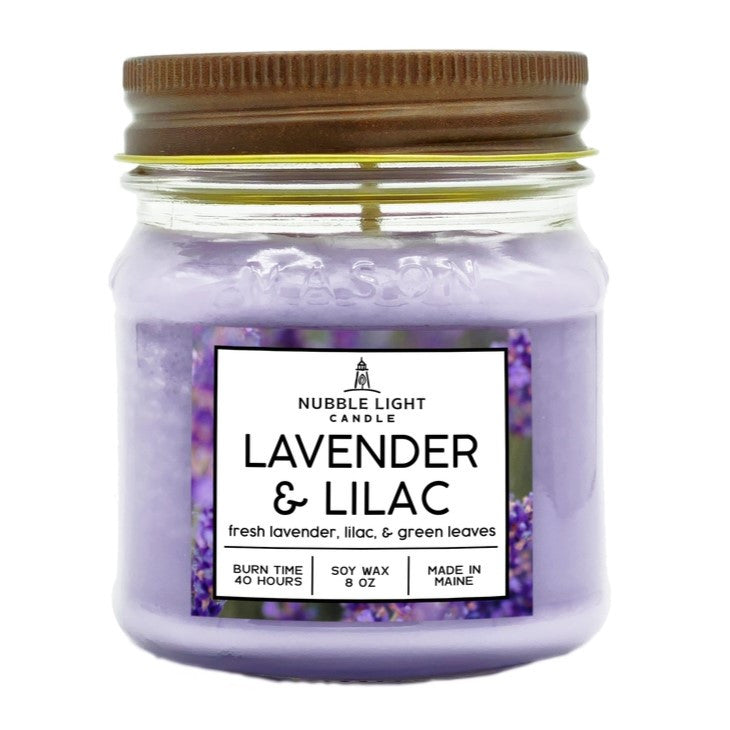 a candle in a clear glass mason jar with light purple wax and a label that reads "Lilac & Lavender" against a white background