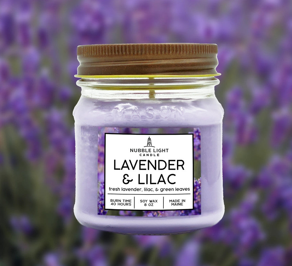 a candle in a clear glass mason jar with light purple wax and a label that reads "Lilac & Lavender" against a soft image of a lavender field