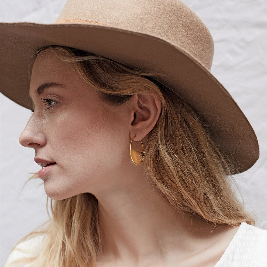 a pair of gold hoop earrings that form a half circle like a half full moon on a model