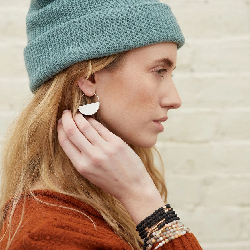 a pair of silver hoop earrings that form a half circle like a half full moon on a model