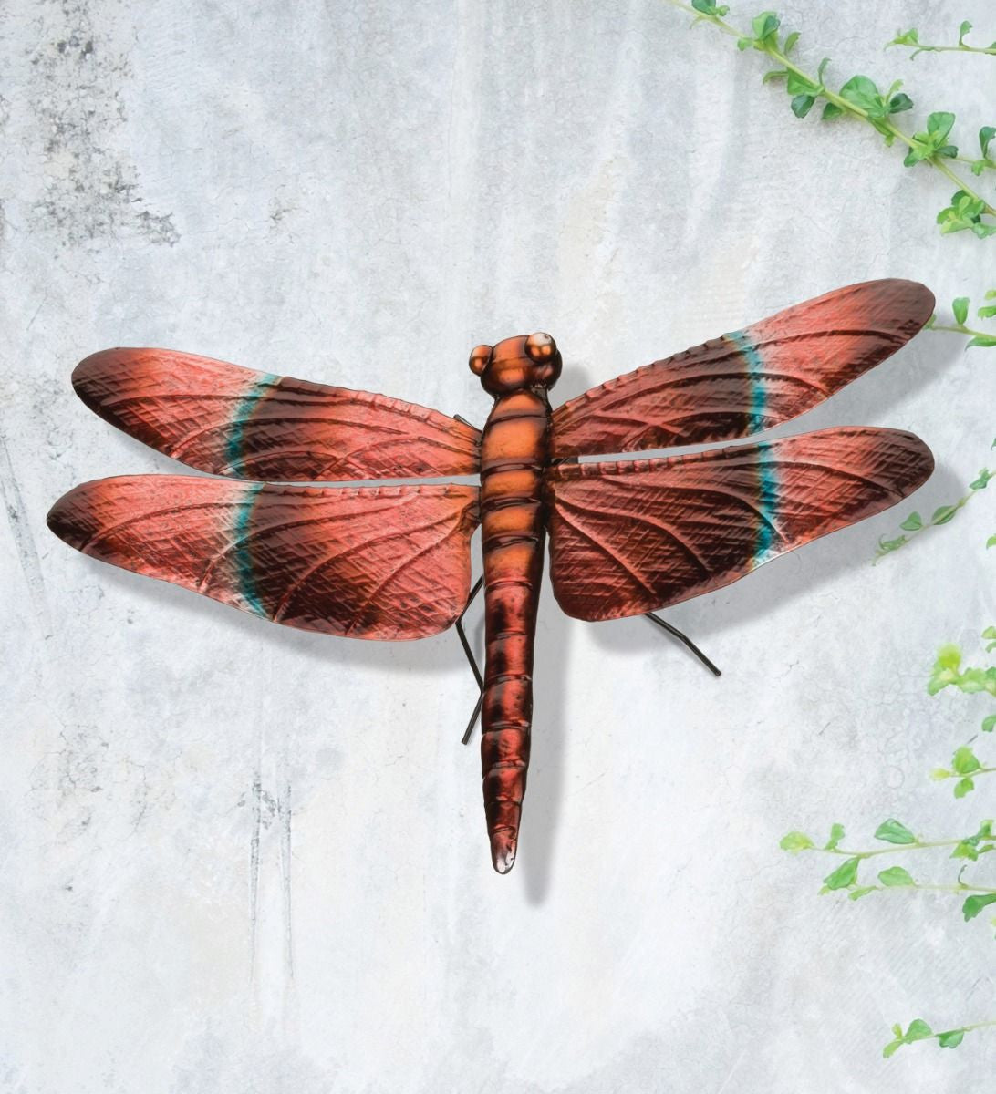 the meadowhawk dragonfly without the stake and displayed hanging on a gray concrete wall with some surrounding greenery to show an alternate decor method