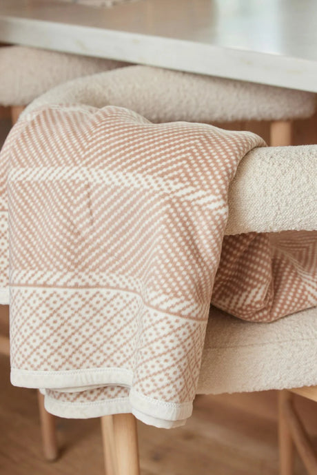 An Old Port Herringbone Tan blanket draped over the arm of a chair