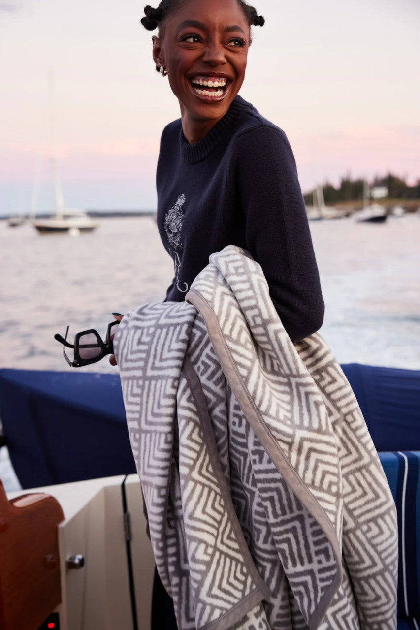 a smiling model on a boat with the blanket draped over her arm, in the background the sea and other sailboats are visible