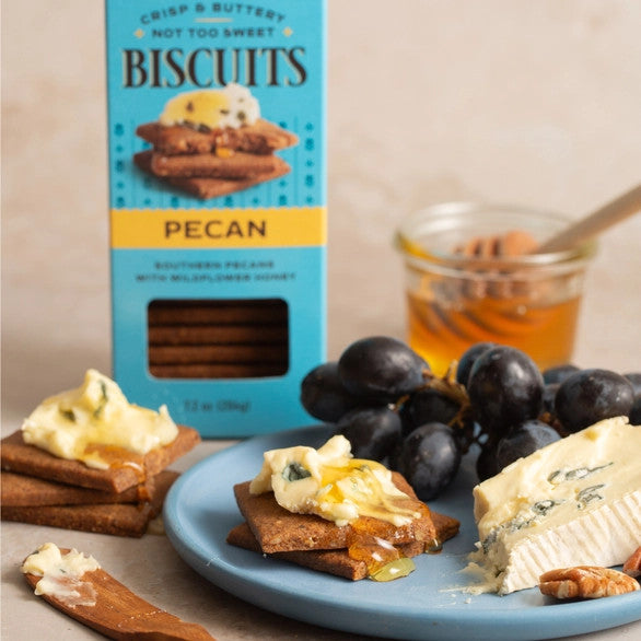 a tasty tabletop spread featuring a box of pecan biscuits near a plate with grapes, cheese, honey, and biscuits