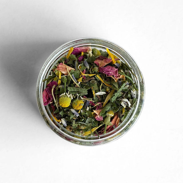 a top view of a circular glass jar filled with beautiful, colorful tea made of herbs and flowers