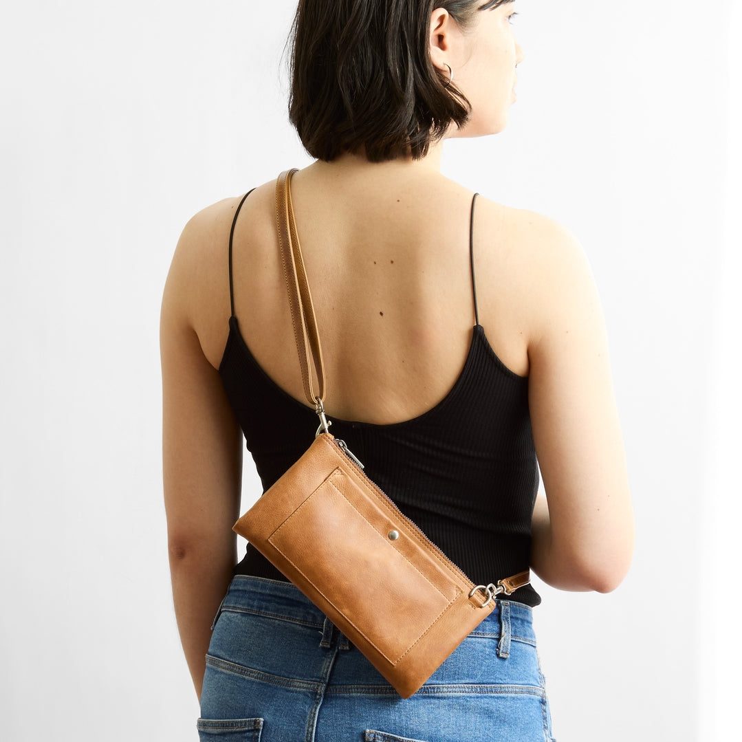 Woman wearing a brown leather crossbody bag on a plain background