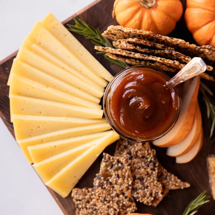 a close up above view of a circular charcuterie board with cheeses, nuts, fruit, and an open jar of pumpkin butter