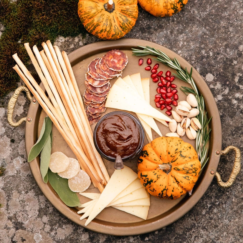 an above view of a circular charcuterie board with cheeses, nuts, fruit, and an open jar of pumpkin butter