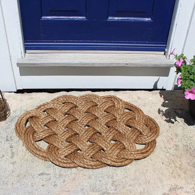 a hand woven rounded nautical door mat with intricate pattern in front of a blue door