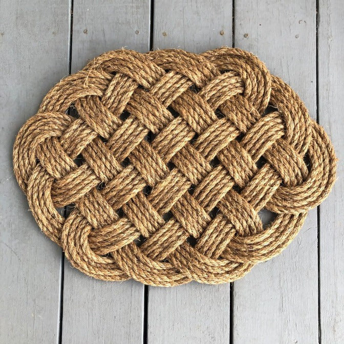 a hand woven rounded nautical door mat with intricate pattern on a gray wooden dock