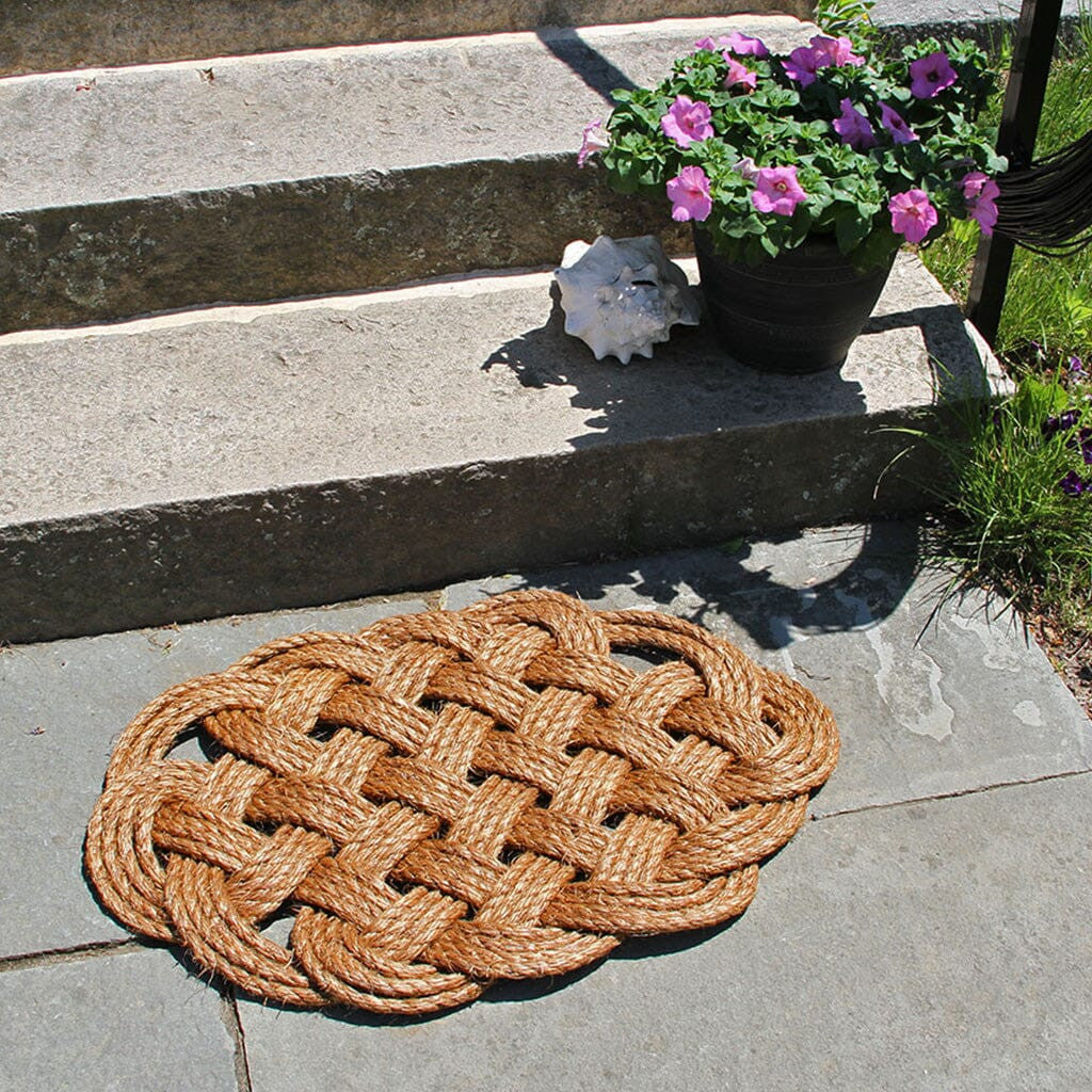 a hand woven rounded nautical door mat with intricate pattern in front of steps