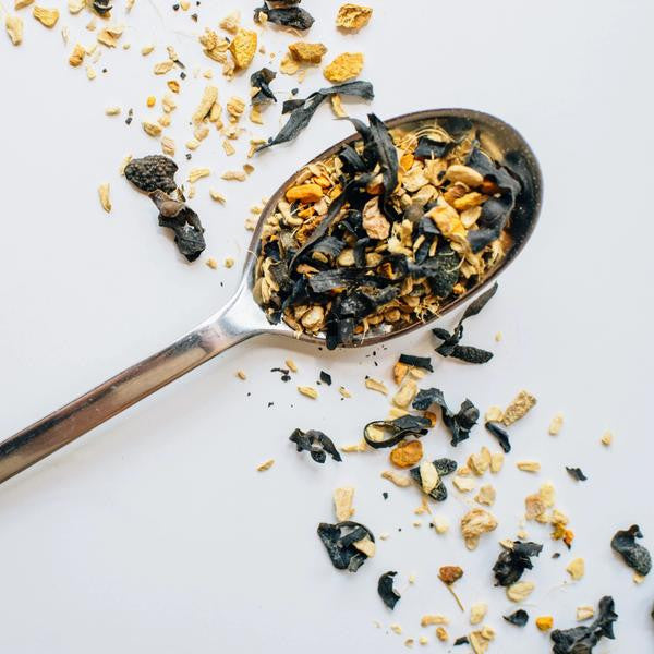 a silver spoon with a heap of sailor's cure all loose leaf tea on a white surface with a diagonal band of loose leaf tea sprinkled across it