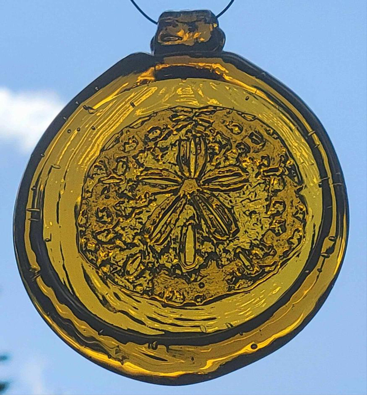a round amber yellow glass sun catcher with relief image of a sand dollar