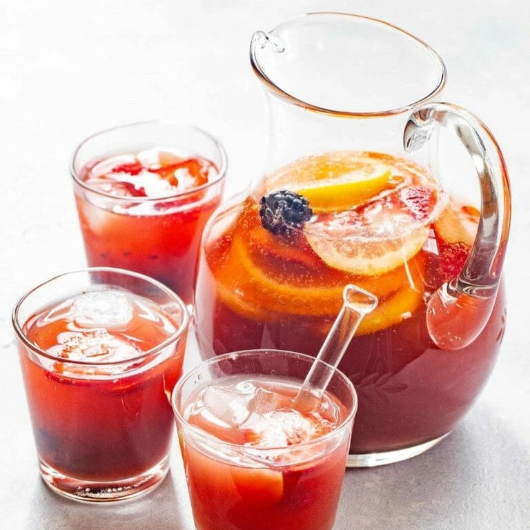 a clear glass pitcher of sangria and fresh fruit alongside 3 glasses of sangria
