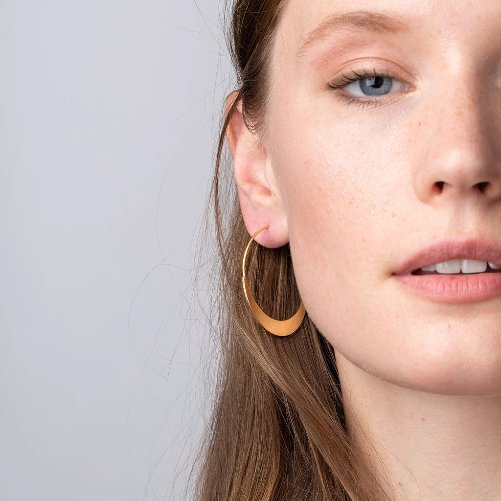 a model wearing the gold crescent hoop earrings