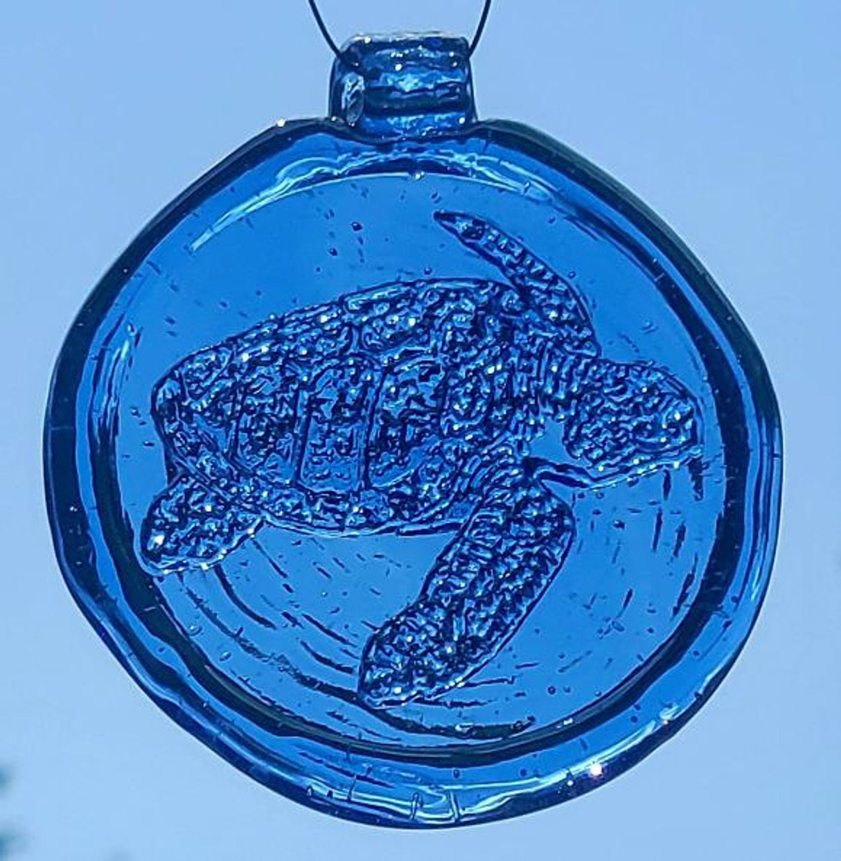 a round blue glass sun catcher with relief image of a sea turtle