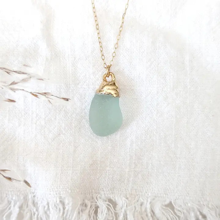 a delicate piece of aqua colored sea glass dipped in gold and suspended from a gold chain
