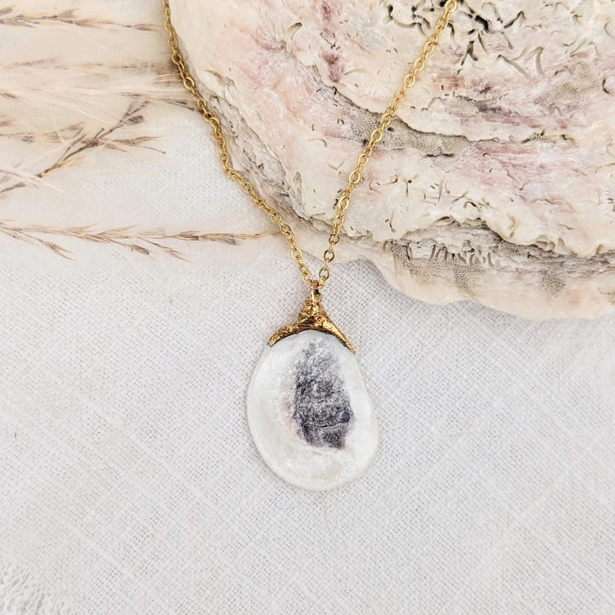 a delicate gold chain with a real oyster shell charm that is dipped in 14k gold where is attaches to the chain