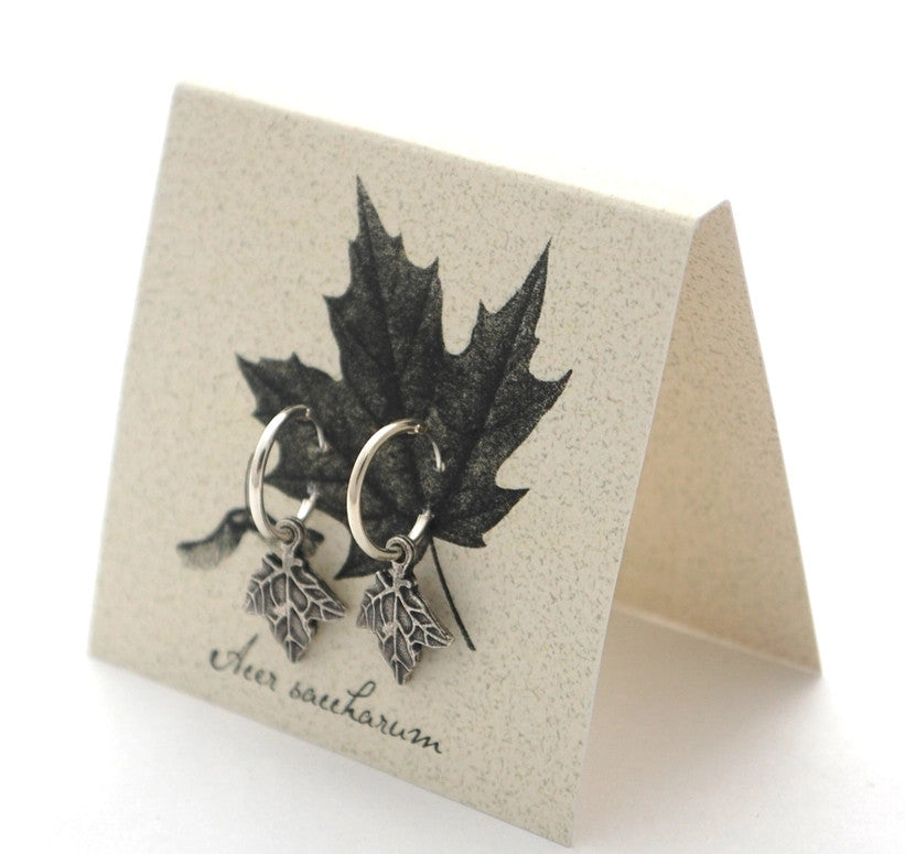 silver maple hoop earrings on an off white backer card printed with a black and gray illustration of a maple leaf