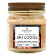 a candle in a clear glass mason jar with tan wax and a label that reads "White Mountains Ski Lodge" against a white background