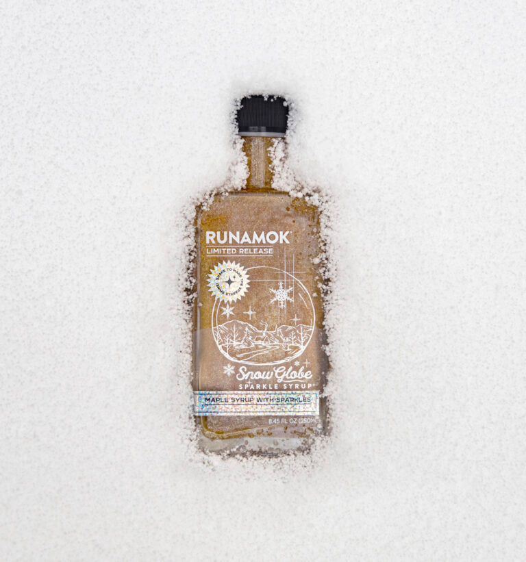 snow globe maple syrup bottle resting atop a blanket of snow to show the wintry magic of this syrup