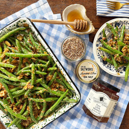 a table spread with a baked green bean dish alongside an open jar of summer citrus sea salt