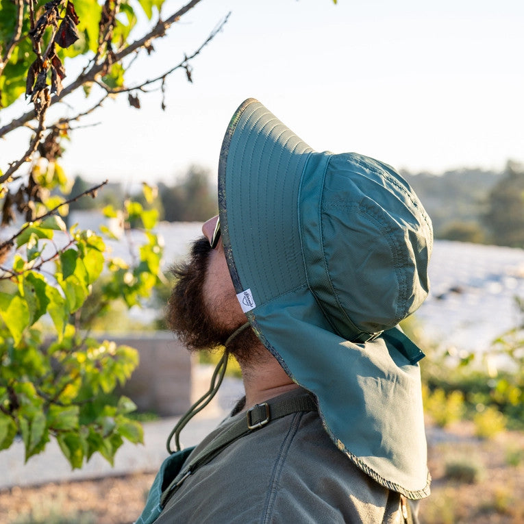 a model facing away from the viewer and wearing the Green Brush Camo Sun Hat with the neck flap covering their neck and upper back