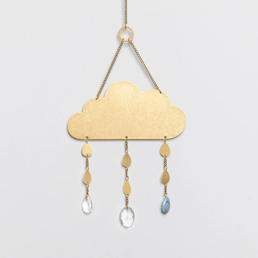 an elegant and minimal suncatcher in brass in the shape of a simple cloud with 3 gems hanging below it mimicking raindrops
