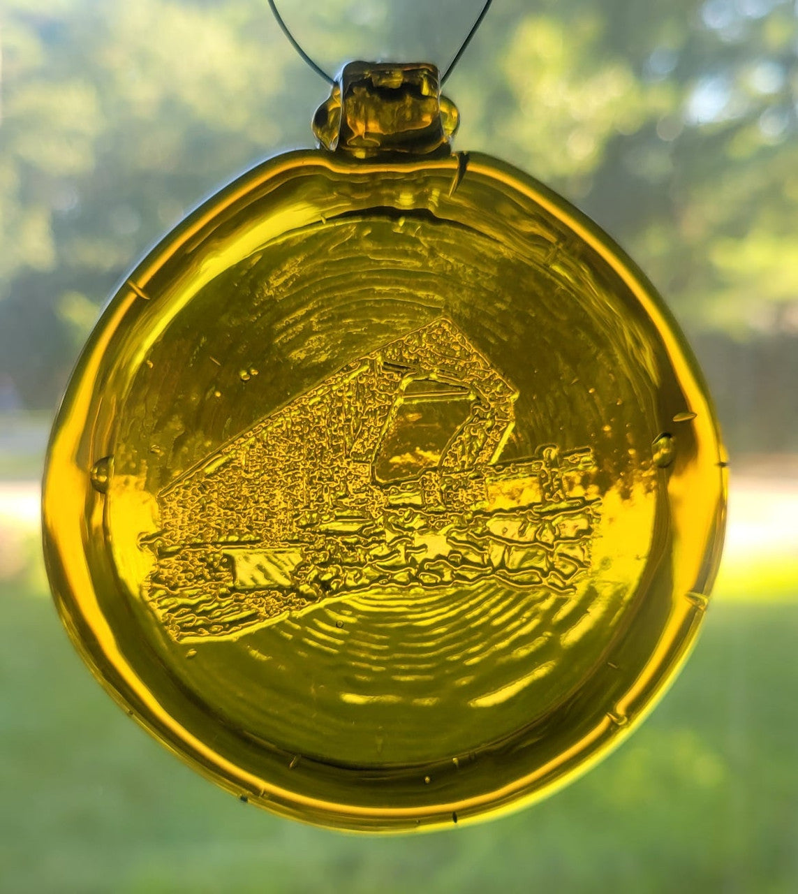 Yellow glass suncatcher with a covered bridge design.