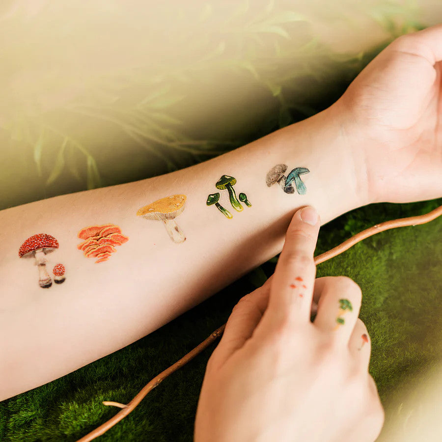 closeup of a model's inner forearm with multiple colorful mushroom tattoos applied in a line