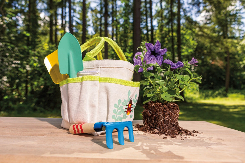 kids garden tote and tools on a table outdoors next to some flowers ready to be potted