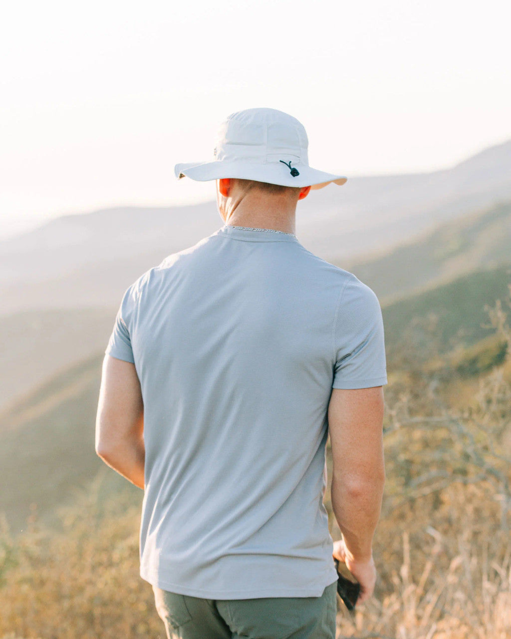 a model wearing the venture sun hat on a hill side with their back to the viewer