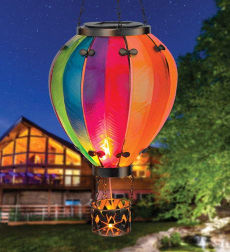 Colorful hot air balloon-shaped solar light glowing at night, hanging in front of a house and trees.