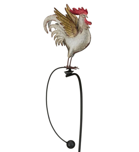 a farther photo of A metal garden stake featuring a colorful rooster with detailed feathers, perched on a rocker that moves in the wind.