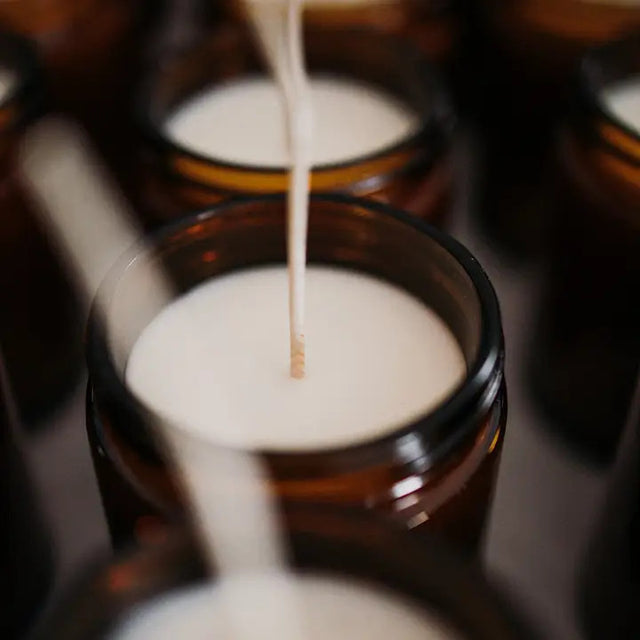 production shot of several candles in their amber glass jars with the lids off revealing the white soy wax and long wicks prior to being cut