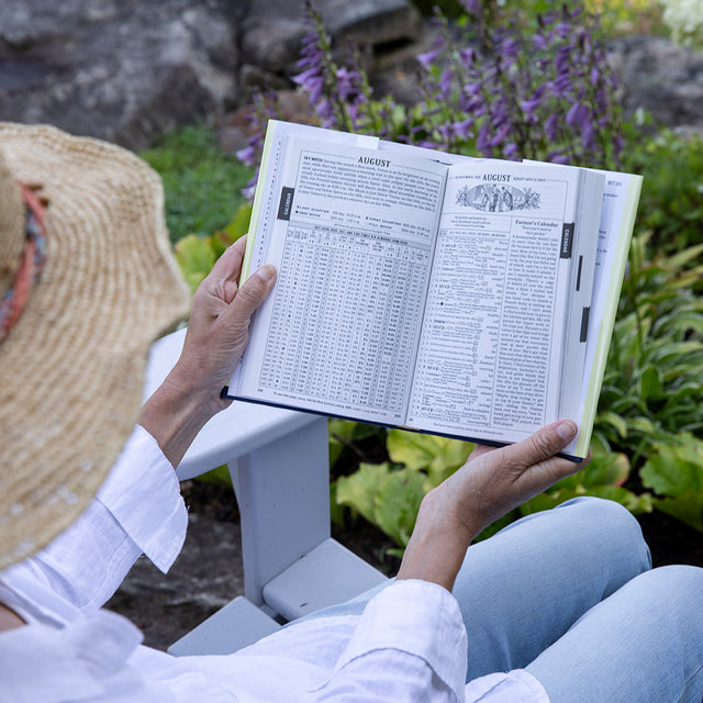 Gardener reading the Old Farmer's Almanac Collector's Edition in a flower garden.