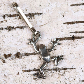 a handcrafted pewter tree frog zipper pull laid on a piece of white birch bark and posed as if it is climbing the tree