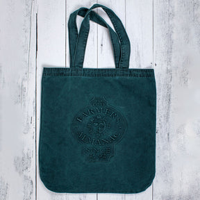 on rustic white wood lays a dark green, oversize tote with the Old Farmer's Almanac sun face logo embossed on the center of the bag