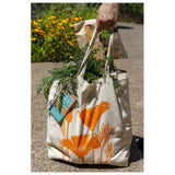 the farmer's market tote outdoors filled with overflowing grocery items with the orange poppy side showing