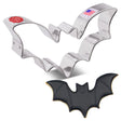 A tin cookie cutter in the shape of a flying bat with wings spread next to a fully decorated bat cookie with black icing, wing detail, and a cute smiling face