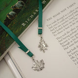 A pewter bookmark in the shape of a leaf attached to a ribbon, resting on an open book.