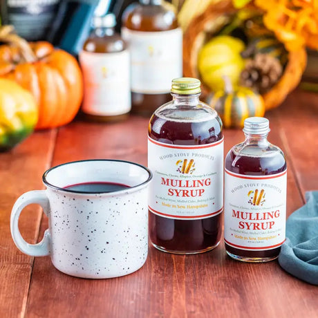 an autumnal tabletop covered with pumpkins and gourds and two bottles of mulling syrup alongside a mug of a tasty mulled beverage